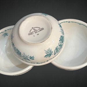 May include: Three white ceramic bowls with green maple leaf designs. The bottom bowl has the text "Liberty Albert Pick Co. Chicago, Ill.  T III" printed on the bottom.