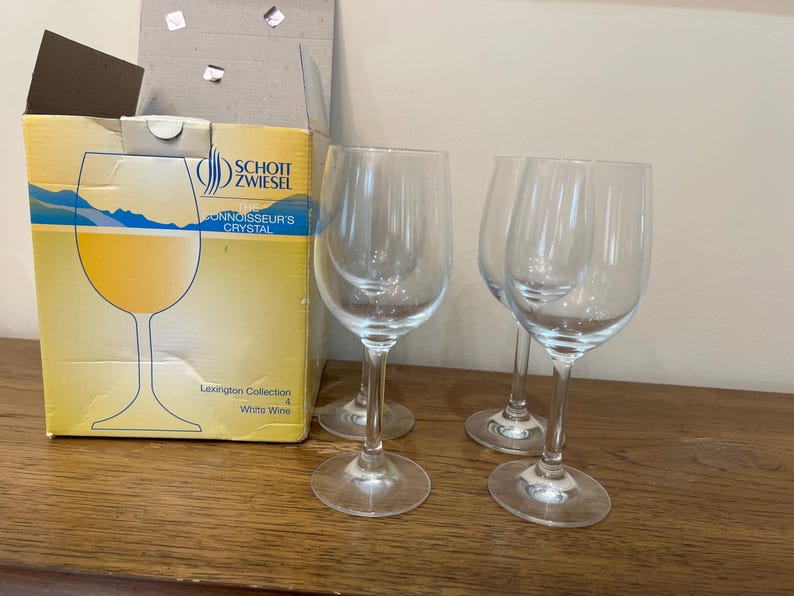 K&ouml;nnte beinhalten: Vier klare Weingl&auml;ser aus Glas auf einer Holzoberfl&auml;che. Die Gl&auml;ser sind alle gleich gro&szlig; und haben die gleiche Form, und sie sind alle leer. Die Gl&auml;ser sind in einer Reihe angeordnet, wobei das erste Glas in der Reihe etwas n&auml;her am Betrachter ist als die anderen drei. Die Gl&auml;ser sind alle aus klarem Glas und haben einen leicht abgerundeten Boden. Die Gl&auml;ser sind alle leer und sauber.