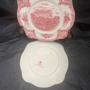 Może przedstawiać: Biały ceramiczny talerz z różowym wzorem kwiatowym i obrazkiem zamku. Na odwrocie talerza widnieją słowa "Johnstone & Wright" i "Old Ashton Castle" w kolorze różowym.
