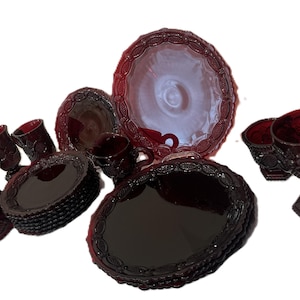 以下が含まれることがあります： ルビーレッドのガラス製品のコレクション。皿、カップ、ボウル、ステムグラスなど。縁にはテクスチャ加工された装飾的なデザインが施されています。このセットはおそらく、食べ物や飲み物を提供するためのものです。