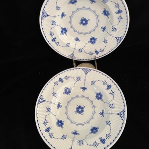 Può includere: Due ciotole per zuppa in ceramica bianca con motivi floreali blu. Le ciotole hanno un bordo ondulato e un bordo rialzato.