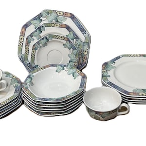Könnte beinhalten: Ein komplettes weißes Porzellan-Tafelservice mit einem dekorativen Blattmuster in Blau-, Grün- und Brauntönen. Das Set umfasst Tassen, Untertassen, Teller, Schalen und eine Butterdose. Die Teller und Schalen haben eine achteckige Form.