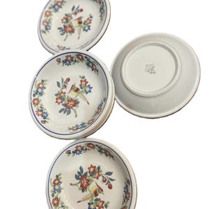 May include: Four white ceramic bowls with a floral and bird design. The bowls have a blue rim and feature red, blue, and yellow flowers and birds. One bowl is upside down, revealing a stamp on the bottom.