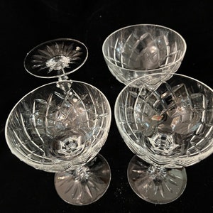 May include: Four clear glass champagne coupes with a cut glass pattern. The coupes are arranged in a square shape.