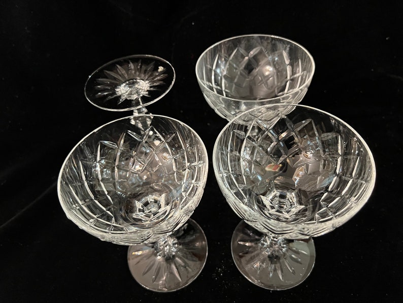 May include: Four clear glass champagne coupes with a cut glass pattern. The coupes are arranged in a square shape.
