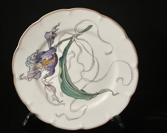 Peut inclure: Une assiette en porcelaine blanche avec un bord doré présente un motif peint à la main d'une orchidée violette avec des feuilles vertes et des rubans blancs.