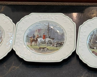 May include: Three white ceramic square plates with raised edges and a green border. Each plate features a different hunting scene with riders on horseback and hounds.
