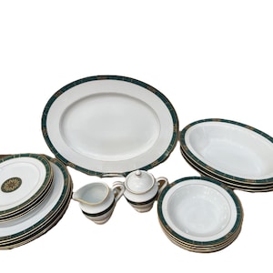 Puede incluir: Un juego de vajilla de porcelana blanca con borde verde y dorado. El juego incluye platos, cuencos, fuentes, una lechera y una azucarera. Los platos tienen un diseño floral dorado en el centro.