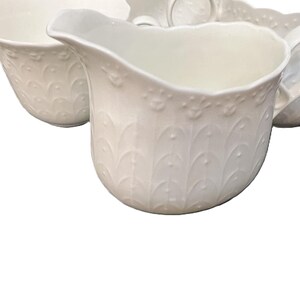 May include: A set of white porcelain serving items, including a creamer, bowls, and plates. The creamer features a handle and an embossed decorative pattern. The items are arranged on a white background, suitable for a formal dining occasion.