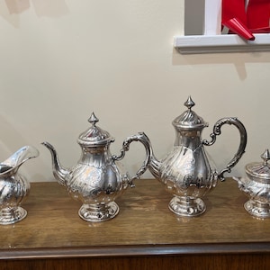 Peut inclure: Un service à thé en argent composé d'une théière, d'un pot à crème, d'un sucrier et d'une deuxième théière. Le service à thé est orné de motifs détaillés et a une finition polie.