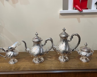 May include: A silver tea set with a teapot, creamer, sugar bowl, and a second teapot. The tea set is ornate with detailed designs and has a polished finish.