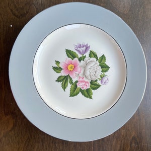 May include: A white ceramic dinner plate with a blue rim and a floral design featuring pink, white, and purple flowers.