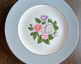 May include: A white ceramic dinner plate with a blue rim and a floral design featuring pink, white, and purple flowers.