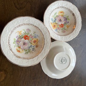 May include: Three white ceramic bowls with a floral design and gold trim. The bowls are nested inside each other. The bottom bowl has the text "The Edwin M. Knowles China Co. Made in U.S.A." printed on the bottom.