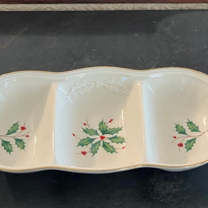 Può includere: Un piatto da portata in ceramica bianca con tre sezioni. Ogni sezione ha un bordo dorato e un motivo di foglie di agrifoglio verdi con bacche rosse.