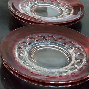May include: Two clear glass plates with a raised, scalloped edge and a burgundy rim. The plates are stacked on top of each other.