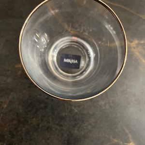 Könnte beinhalten: Ein klares Glas Trinkglas mit goldfarbenem Rand. Das Glas hat den Schriftzug "Mikasa" auf dem Boden.