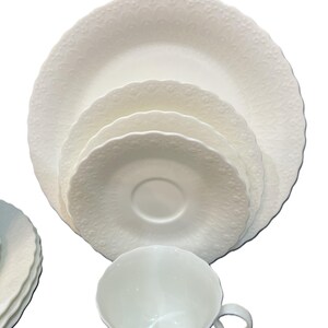 May include: A white porcelain tea set comprising a cup, saucer, and plates. The set includes a teacup, a saucer, and several plates of varying sizes. The edges of the plates and cup have a scalloped design.