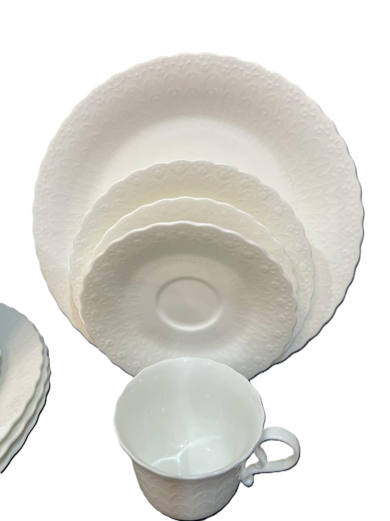 May include: A white porcelain tea set comprising a cup, saucer, and plates. The set includes a teacup, a saucer, and several plates of varying sizes. The edges of the plates and cup have a scalloped design.