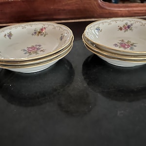 May include: Two sets of four white porcelain soup bowls with floral patterns and gold trim. The bowls are stacked on top of each other.