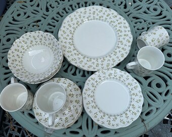 May include: A set of white ceramic dishes with a green floral pattern. The set includes a bowl, a plate, a saucer, and a cup.