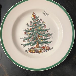 Könnte beinhalten: Ein weißer Keramikteller mit grünem Rand. Der Teller zeigt eine detaillierte Illustration eines geschmückten Weihnachtsbaums mit Ornamenten, Geschenken und dem Weihnachtsmann. Ein festliches Urlaubsdesign.