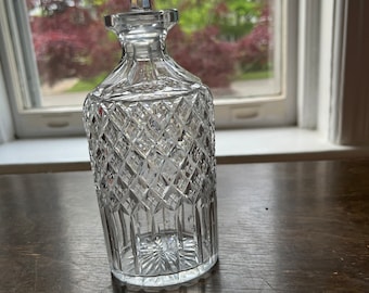 May include: A clear glass decanter with a diamond pattern and a crystal stopper. The decanter is sitting on a wooden surface.