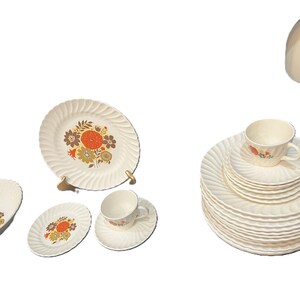 May include: A collection of cream-colored vintage dishware with a floral design in orange, brown, and green. The set includes plates, saucers, and teacups, showcasing a classic, retro aesthetic. The plates have a ridged edge.