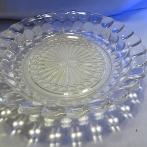 May include: A clear glass plate with a raised, textured rim and a center design of radiating lines and circles.