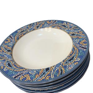 Könnte beinhalten: Ein Stapel von sechs weißen Keramiktellern. Jeder Teller hat ein blaues Mosaikmuster am Rand, mit Blautönen, Gelb und Orange. Die Teller haben ein schlichtes, elegantes Design.