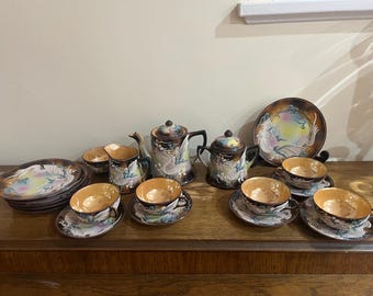 Może przedstawiać: Zestaw do herbaty w stylu vintage z motywem smoka. Zestaw zawiera czajnik, dzbanek na śmietanę, cukiernicę i sześć filiżanek do herbaty i spodków. Filiżanki do herbaty i spodków są ozdobione białym smokiem na brązowym tle.