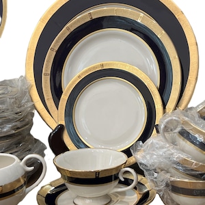 Può includere: Elegante set di stoviglie con dettagli blu navy e oro. Il set include piatti di varie dimensioni, tazze da tè, piattini e una lattiera. Ogni pezzo ha un bordo dorato e una fascia blu navy, creando un look sofisticato per la tavola.