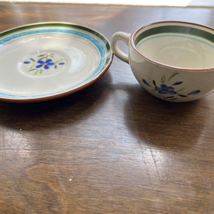May include: A white ceramic teacup and saucer with a blue and green floral design. The saucer has a blue and green border.