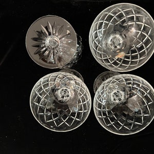May include: Four clear glass goblets with a cut crystal design. The goblets are arranged in a square pattern on a black surface.