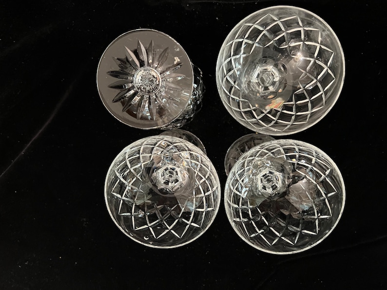 May include: Four clear glass goblets with a cut crystal design. The goblets are arranged in a square pattern on a black surface.
