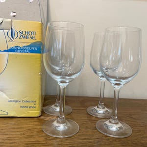 K&ouml;nnte beinhalten: Drei klare Weingl&auml;ser aus Glas mit dickem Boden und breitem Kelch. Die Gl&auml;ser stehen auf einer Holzoberfl&auml;che. Der Karton im Hintergrund ist gelb und tr&auml;gt den Aufdruck "Schott Zwiesel The Connoisseur's Crystal Lexington Collection White Wine".