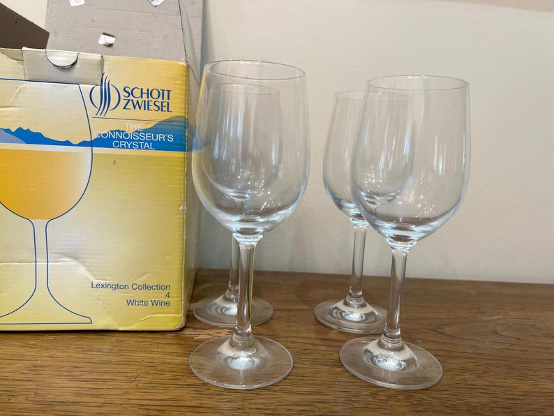 K&ouml;nnte beinhalten: Drei klare Weingl&auml;ser aus Glas mit dickem Boden und breitem Kelch. Die Gl&auml;ser stehen auf einer Holzoberfl&auml;che. Der Karton im Hintergrund ist gelb und tr&auml;gt den Aufdruck "Schott Zwiesel The Connoisseur's Crystal Lexington Collection White Wine".