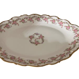 Puede incluir: Fuente ovalada con borde festoneado y ribete dorado. El plato de porcelana blanca está decorado con un motivo floral de rosas rosas y hojas verdes. Un diseño floral central refleja el borde.