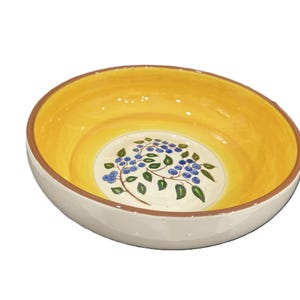 May include: A round ceramic bowl with a bright yellow interior and a white exterior. The center of the bowl features a hand-painted design of blue berries on brown stems with green leaves. The rim of the bowl is finished with a thin brown line.