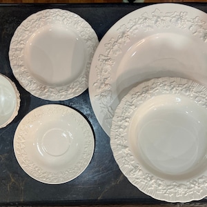 May include: A set of white porcelain dishes with a raised floral design. The set includes a large platter, a medium-sized bowl, a small plate, and a teacup and saucer.