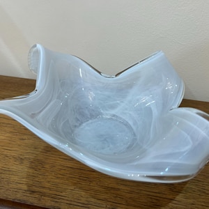 May include: A white glass bowl with a wavy, organic shape. The bowl has a smooth, glossy finish and a delicate, swirling pattern.