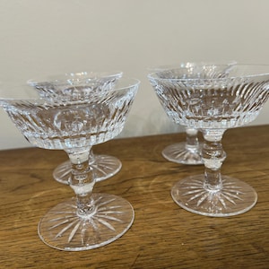 Może przedstawiać: Cztery przezroczyste szklane kieliszki do szampana z wygrawerowanym wzorem. Kieliszki ustawione są na drewnianej powierzchni.