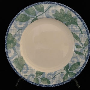May include: A white ceramic dinner plate with a blue and green leafy pattern. The plate has a white rim and a blue and green border.