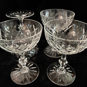 May include: Four clear glass champagne coupes with a cut glass design. The coupes are arranged in a square formation.