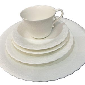 May include: A white porcelain tea set comprising a teacup, saucer, small bowl, and two plates. The set features a textured floral design and a scalloped edge. Ideal for serving tea.