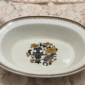 May include: White oval serving dish with a black and gold floral design. The dish has a fluted edge and a gold rim.