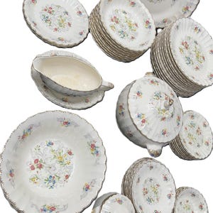 Könnte beinhalten: Eine Sammlung von Vintage-Geschirr aus weißem Porzellan mit floralem Design. Das Set umfasst Teller, Schalen, eine Sauciere und eine Servierschüssel mit Deckel. Jedes Stück hat einen Goldrand und einen gewellten Rand.