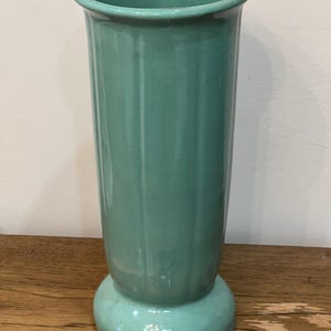 May include: A tall, slender, light green ceramic vase with a flared base. The vase has a smooth, glossy finish and a simple, elegant design.