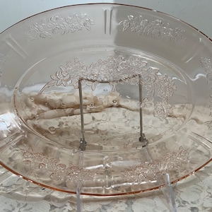 May include: A pink glass oval serving platter with a raised floral design. The design features roses and leaves.