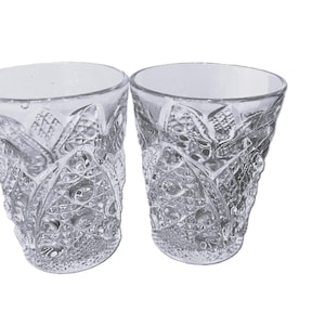 Puede incluir: Dos vasos transparentes de cristal tallado con intrincados patrones geométricos. Los vasos tienen una boca ancha y un exterior texturizado, mostrando una estética vintage. Perfectos para servir bebidas.
